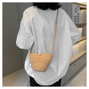 Straw crossbody bucket bag with pearl detail and rope strap shown on a model