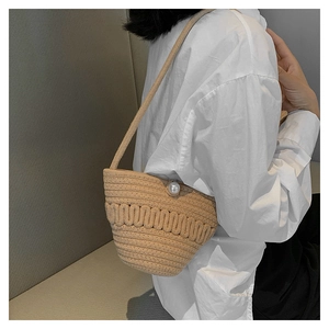 Close-up of beige woven crossbody straw bag with wave patterns and a large pearl bead