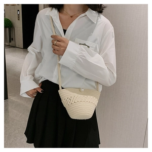 Detail of beige hand-woven straw crossbody bag featuring unique wave texture and pearl button