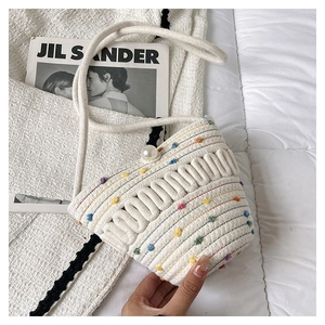 Detail of woven bucket bag with colorful pom-poms and a large pearl button closure