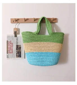 Detail of the woven straw tote showing green, beige, and blue striped texture