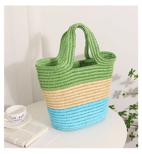 Detail of a large woven straw tote bag with green, beige, and blue striped panels