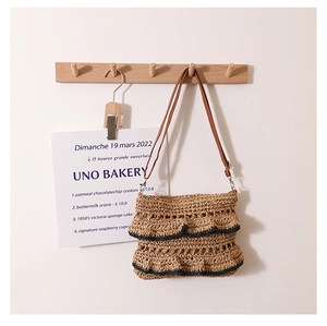 Détail d'un sac en paille à volants et bords noirs suspendu dans un décor bohème