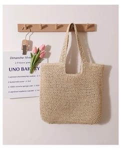 Detail of hand-woven beige straw tote bag hanging on a wooden hook in a natural scene