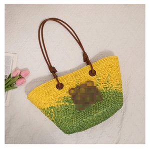 Détail d'un sac cabas en paille jaune et vert avec anses en cuir marron et fleurs
