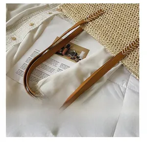 Detail of straw tote bag with brown leather shoulder strap and white V-shaped stitching
