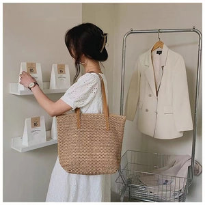 Detail of a large straw tote bag with brown leather straps on a white summer dress