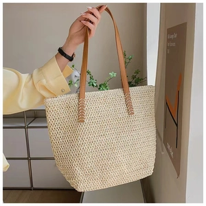 Detail of hand-woven straw tote bag with brown leather straps and cross-stitch detail