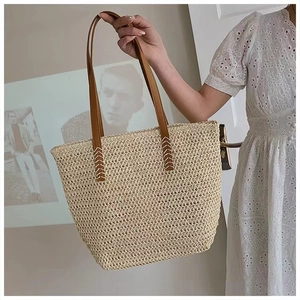 Close-up of beige woven straw tote with brown leather strap and contrast cross-stitching