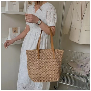 Detail of the woven straw tote bag featuring brown leather handles and hollow weave style