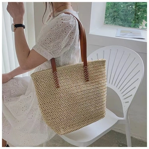 Close-up of a straw tote bag showing tight diamond weave and brown handles with X-shaped stitching