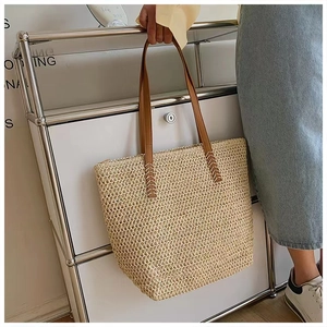 Detail of handwoven straw tote bag with brown leather straps and cross-stitch reinforced handles