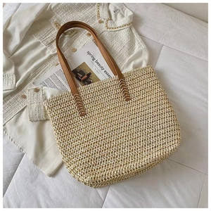 Detail of hand-woven straw tote bag featuring brown leather straps on a white backdrop