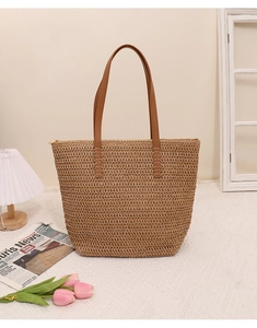 Close-up of woven straw tote bag with brown PU leather handles and zipper closure