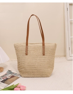 Close-up of the woven straw texture and durable brown shoulder straps on a beige tote bag