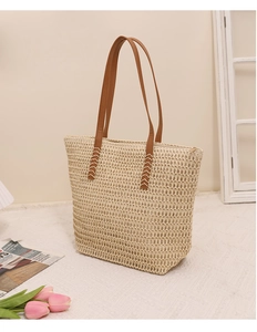 Detailed macro view of woven straw tote bag texture and brown faux leather shoulder strap