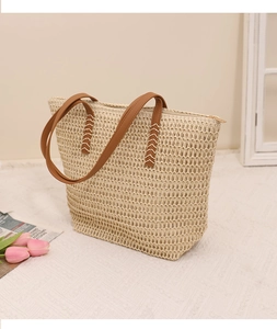 Detail of woven tote bag with brown leather handles and decorative V-shape stitching