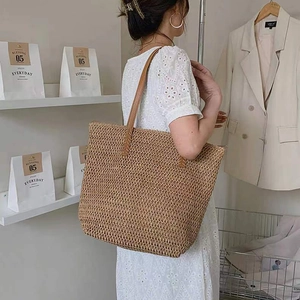 Minimalist straw tote bag with brown leather handles worn by a model in casual style