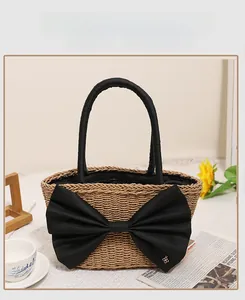 Detail of a beige woven straw bag with a large black fabric bow and round handles