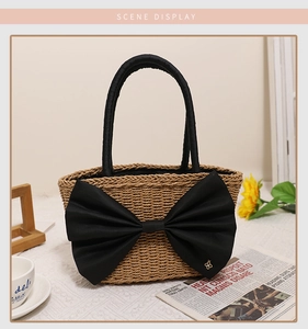 Detail of handmade straw bag featuring a large black bow and golden clover charm decoration