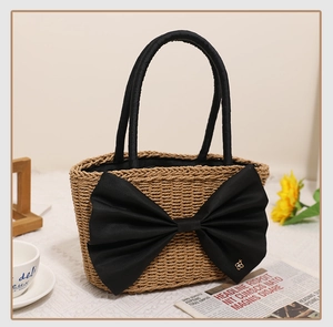 Close-up of handmade straw tote bag with large black silk bow and gold flower buckle detail