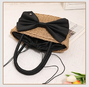 Detail of handmade straw tote bag with large black bow and secure drawstring closure