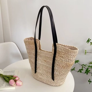 Grand sac cabas en paille tissé à la main avec anses en cuir noir sur table blanche
