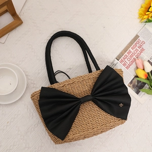 Handwoven straw tote bag with a large black bow and gold buckle on a white textured background