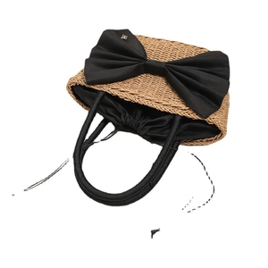 Handmade straw beach handbag with large black bow and round leather handles on white background