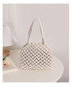 Detail of hollow woven cotton rope handbag with thick twisted handle on a white table