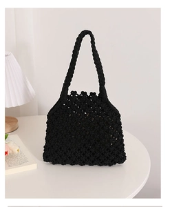 Detail of black hollow woven cotton rope handbag with diamond mesh texture on white table