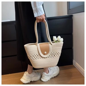 Detail van geweven stro strandtas met bruine lederen flap en parelsluiting
