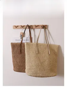 Detail of woven straw tote bags in beige and brown hanging on a wooden rack