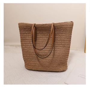 Detail of hand-woven straw tote bag featuring brown leather handles and natural texture