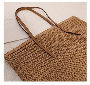Detailed view of the woven texture and brown faux leather strap on a straw tote bag