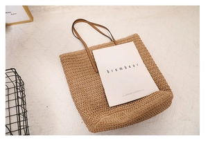 Top view of a beige straw tote bag with brown leather handles on a white textured rug
