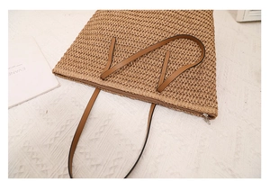 Detailed close-up of brown woven straw tote bag with leather handles and top zipper