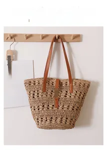 Detail of hollow woven straw tote bag with brown leather handles on wooden hook