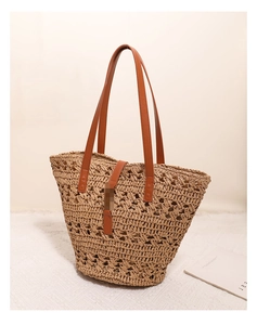 Close-up of woven straw tote bag with brown leather handles and buckle detailing