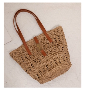 Detail of bohemian woven straw tote bag with brown leather handles and buckle closure