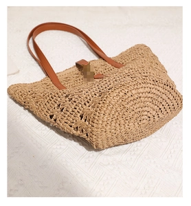 Close-up of woven straw tote bag featuring brown leather shoulder straps and metal buckle