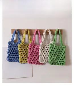 Detailed view of woven cotton hand bags in five vibrant colors hanging on a wooden rack