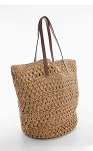 Detail of hollow woven straw tote bag featuring premium brown leather handles and texture
