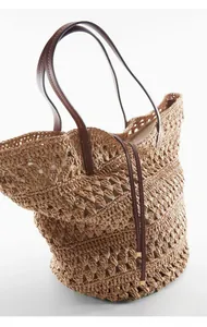 Detail view of large straw tote bag with intricate hollow crochet and brown leather handles
