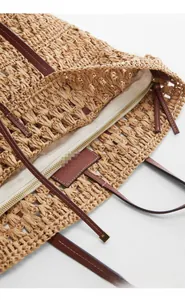 Detail of hollow woven straw tote bag featuring brown leather handle and zipper closure