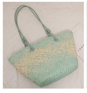 Flat lay of a woven straw tote bag in mint green and beige with leather straps