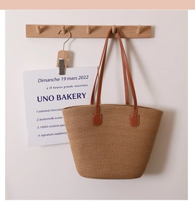 Detail of hand-woven straw tote bag with brown faux leather straps on wooden hanger