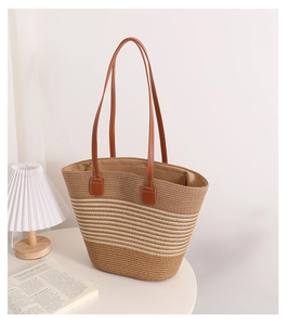 Detail of hand-woven straw tote with brown leather handles on a minimalist white table
