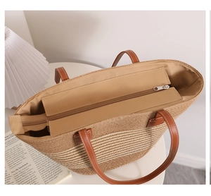 Detail of the woven straw tote bag featuring brown leather handles and secure zip closure