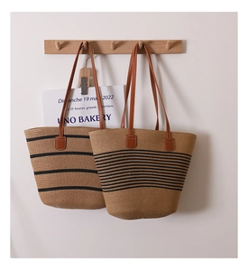 Detail of woven straw tote bags with black stripes and brown leather shoulder straps